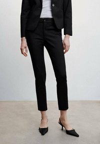 Zwarte op maat gemaakte broek met een slim fit, enkellange snit, gladde textuur en voorzakken, gecombineerd met zwarte puntige hakken.