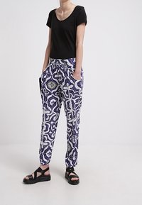 Svart kortärmad topp tillsammans med blå och vita mönstrade byxor med dragsko i midjan och sidofickor, kompletterat med svarta sandaler.