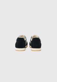 Black suede sneakers with a low profile, cream rubber soles, and contrasting side accents. Features a cushioned interior and rounded toe.