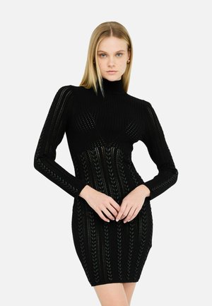 Robe pull noire côtelée avec des manches longues, un col montant et un motif texturé avec des lignes verticales et des motifs de feuilles.