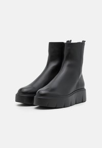 Bottines noires en cuir avec une semelle plateforme épaisse, surface lisse et détails élastiques subtils sur les côtés pour un enfilage facile.