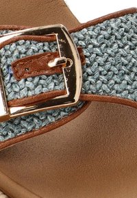 Correa de tela azul tejida con detalles de cuero marrón y una hebilla dorada sobre una plantilla color beige. Tejido texturizado con una base suave.