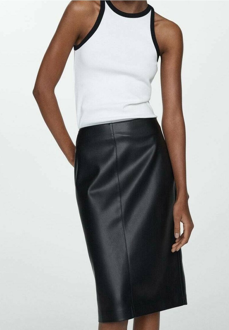 Personne portant un haut blanc sans manches avec bordure noire et une jupe midi en cuir noir taille haute sur un fond uni.