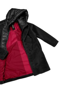 Cappotto nero con cappuccio morbido e trapuntato e un rivestimento rosso brillante. Presenta una texture morbida e chiusure a bottone.