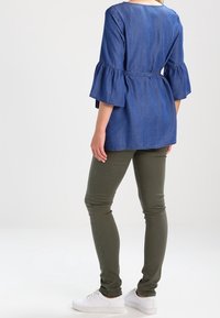 Denim-tunika i blått med utställda ärmar, bälte i midjan, kombinerad med olivgröna skinnybyxor och vita sneakers.