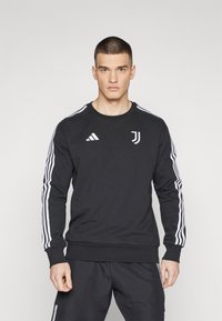 Sort sweatshirt med hvidt Adidas-logo og Juventus-emblem. Har hvide striber på ærmerne, rund halsudskæring og ribbede manchetter.