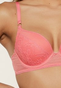 Koraal lace beha met stippenmesh, gevoerde cups en verstelbare bandjes. Voorzien van bloemige kanten details en een gladde afwerking.