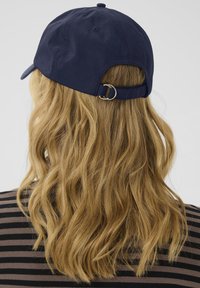 Navy blue baseball cap with a curved brim, adjustable strap featuring a metal ring, and textured fabric, viewed from the back.