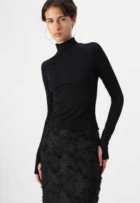 Black long-sleeve turtleneck top with fitted design, smooth texture, and ribbed collar, paired with a black skirt featuring textured floral accents.