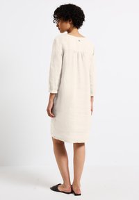Beige Leinenkleid in knie-langer Länge mit dreiviertelärmel, Rückenschlitzdetails und rundem Ausschnitt mit einem kleinen Knopfakzent.