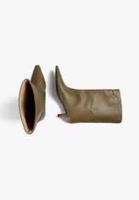 Par de botas de cuero verde oliva hasta la rodilla con punta afilada y tacones bajos en un fondo blanco.