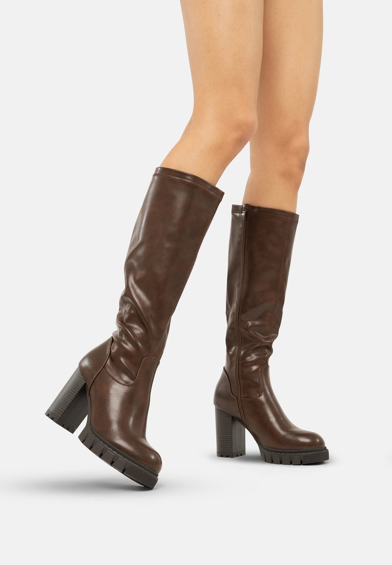 Botas altas de cuero marrón con un tacón grueso, que presentan una textura suave, cremallera lateral y detalles fruncidos en la parte superior.
