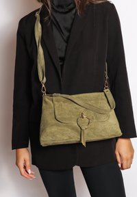 Borsa a tracolla in suede verde oliva con pattina anteriore, dettaglio hardware circolare e tracolla testurizzata. Superficie liscia e forma morbida.