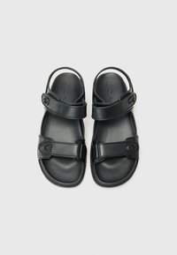 Μαύρες δερμάτινες σάντες με ρυθμιζόμενους ιμάντες, μαλακό πάτο, στρογγυλή μύτη και λογότυπο στις τιράντες. Σχεδίαση με επίπεδη σόλα.