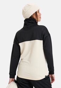 Zwarte en crèmekleurige pullover met een hoge kraag en textuurstof; heeft lange mouwen en een logo op de linkerarm en de onderzoom.