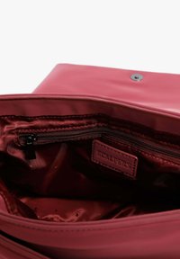 Interior de bolsa de cuero burdeos que incluye un bolsillo con cremallera, forro de satén y una etiqueta de marca. Incluye un cierre a presión en la parte superior.