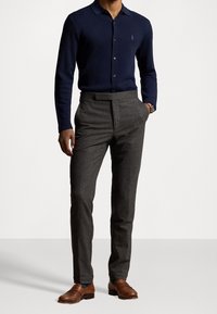 Marinblå långärmad polo med en diskret logotyp, kombinerad med grå texturerade kostymbyxor och bruna läderloafers.