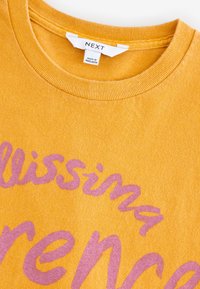 Felpa di cotone giallo senape con scollo arrotondato e collo a coste. Presenta un ampio testo rosa in corsivo sulla parte anteriore.