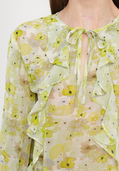 Sheer blouse featuring a floral pattern in yellow and green hues, with ruffled accents and a tie neckline. Smooth, lightweight fabric.