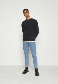 Granatowa bluza z efektem blaknięcia, zestawiona z jasnoniebieskimi dżinsami i czarnymi botkami na sznurowadła. Wyjątkowy wygląd podkreślają przezroczyste okulary.