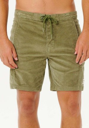 Man draagt olijfgroene corduroy korte broek met voorzakken en een aantrekkoord in de taille, staat met ontspannen handen langs het lichaam.