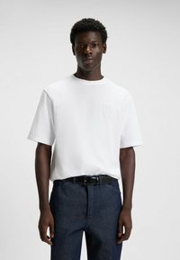 Hvid bomulds T-shirt med rund hals og korte �ærmer, prydet med et tonalt prægede "HUGO" logo på venstre bryst. Kombineret med mørke denim bukser.