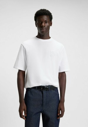 White cotton T-shirt with a crew neck and short sleeves, featuring a tonal embossed "HUGO" logo on the left chest. Paired with dark denim trousers.
