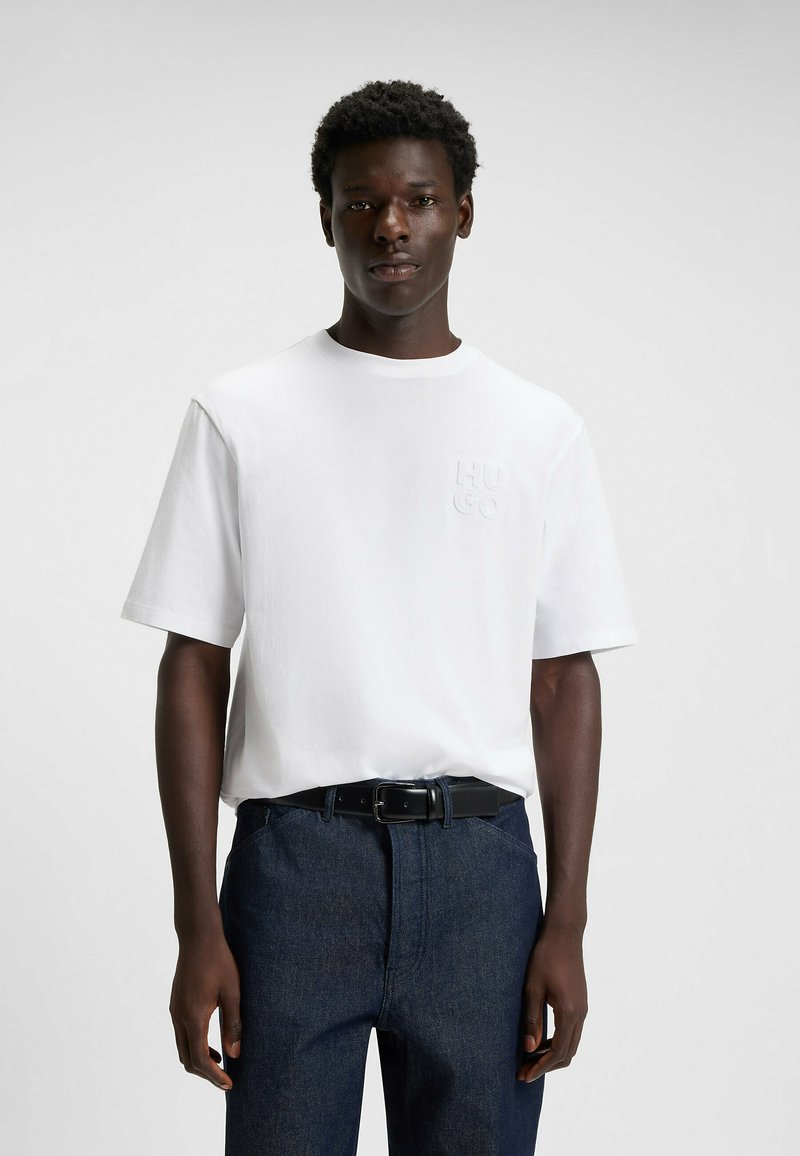 Hvid bomulds T-shirt med rund hals og korte ærmer, prydet med et tonalt prægede "HUGO" logo på venstre bryst. Kombineret med mørke denim bukser.