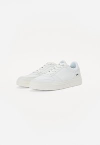 Hvite sneakers med en glatt læroverdel, rund tå og perforerte detaljer. Har flate lisser og logo på siden.