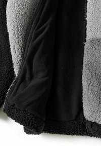 Veste en polaire avec un design noir, gris et texturé, dotée d'une doublure douce. La fermeture éclair et les poignets en peluche améliorent la chaleur et le confort.