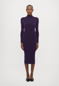 Violetti pitkähihainen, korkean kauluksen mekko, joka on valmistettu neulekankaasta, istuva siluetti, polven mittainen, käytössä mustien tasapohjaisten kenkien kanssa.