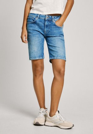 Heledsinised denimsärgiga lühikesed püksid, tavalise vöökohaga ja õmblustega äärega, sobitatud beežide tossude ja valge lühikese toppiga.