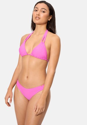 Mujer con un bikini halter de color rosa brillante y parte inferior a juego, posando frente a un fondo liso de color gris claro.