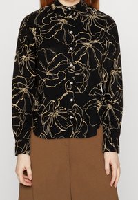 Svart skjorta med knappar som har ett beige blommönster, tillverkad av ett mjukt material, med långa ärmar och en klassisk kraging.