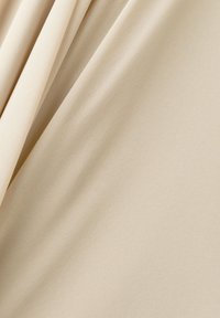 Světlý béžový textil s hladkým povrchem, zdobený jemnými, nenápadnými vzory. Uložený v měkkých záhybech, vytvářející různorodé odstíny barev.