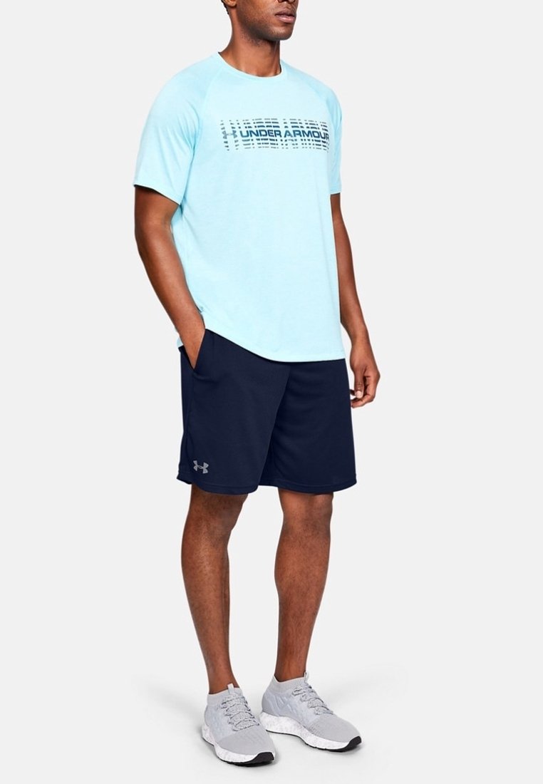 Ljusblå atletisk T-shirt med "Under Armour"-logotyp, i kombination med marinblå shorts och grå löparskor. Slätt tyg, avslappnad design.