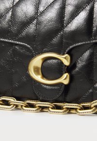 Schwarze, gesteppten Lederhandtasche mit einem auffälligen goldenen C-förmigen Verschluss und goldenen Kettendetails am Boden, ausgestattet mit einer strukturierten Oberfläche und elegantem Design.