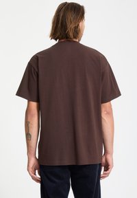 T-shirt en coton marron avec une coupe décontractée, des manches courtes et un col rond. Texture lisse, sans motifs ni accents visibles.