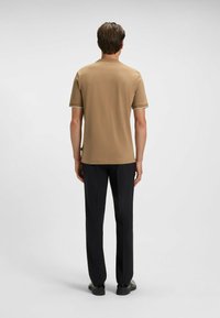 Light brown short-sleeve shirt with white trim at cuffs, paired with black tailored trousers. Smooth texture and straight-fit design.