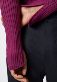 Fitted ribbed knit sweater in vibrant magenta, with long sleeves and a relaxed cuff. Paired with textured black trousers.