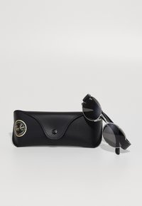 Ray-Ban aurinkolasit mustilla pyöreillä linsseillä ja tyylikkäillä metallikehyksillä, yhdessä tekstuurilla varustetun mustan nahkakotelon kanssa, jossa on kultainen logo.