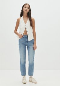Débardeur blanc style halter avec boutons sur le devant, associé à un jean droit bleu clair et des baskets beiges. Design minimal sans motifs.