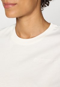 Hvid bomulds T-shirt med rund hals og en diskret præget logo på brystet, med en glat tekstur og afslappet pasform.