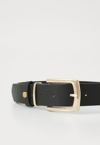 Ceinture en cuir noir avec une boucle en métal doré, texture lisse et un petit détail accent doré près de la sangle d'ajustement.