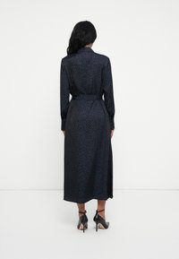 Rochie de culoare navy cu mâneci lungi, imprimată cu leopard, talie strânsă și o siluetă fluidă. Pantofii cu toc înalt negri completează ținuta.