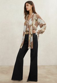 Pruunide ja kreemjate lillemusterlise mustriga pluus, millel on pikad varrukad ja esiküljel lips. Sobitatud kõrge vöökohaga tumedate teksadega, millel on lehvikukujulised sääred.