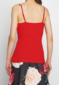 Top rosso senza maniche con spalline sottili, design aderente e texture liscia. Indossato con una gonna a fantasia floreale con grandi fiori bianchi e rosa.