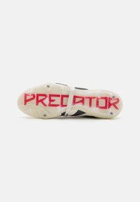 Sort og hvid fodboldstøvle med en tekstureret sål, der har et stort rødt "PREDATOR" print og et hvidt bånd over mellemfoden.