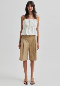 Top cu peplum alb, cu bretele subțiri, asociat cu pantaloni scurți bej până la genunchi. Textură netedă, design casual și detaliu cu șnur la talie.