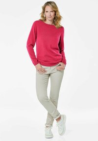 Fuchsia truien met lange mouwen en een ontspannen pasvorm, gecombineerd met lichtbeige broeken en witte sneakers. Vloeiende textuur, casual ontwerp.
